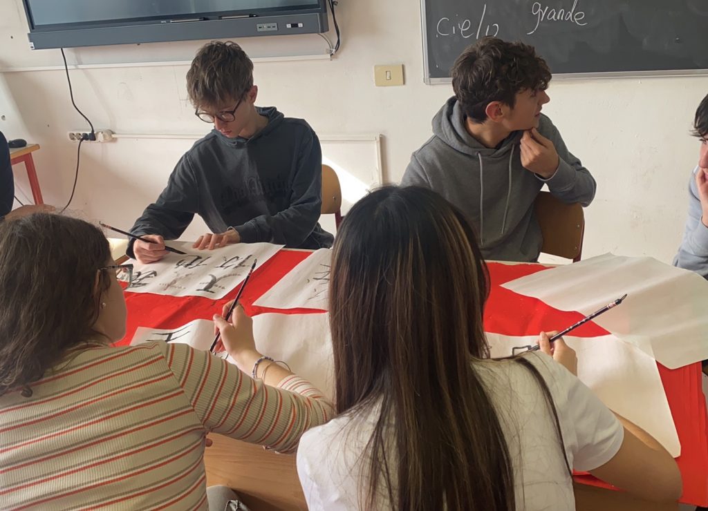 Studenti italiani praticano la calligrafia cinese durante una lezione scolastica a Prato.